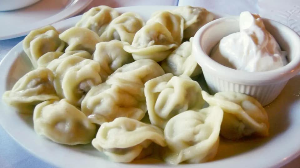 Une assiette de pelmeni servis avec de la crème aigre