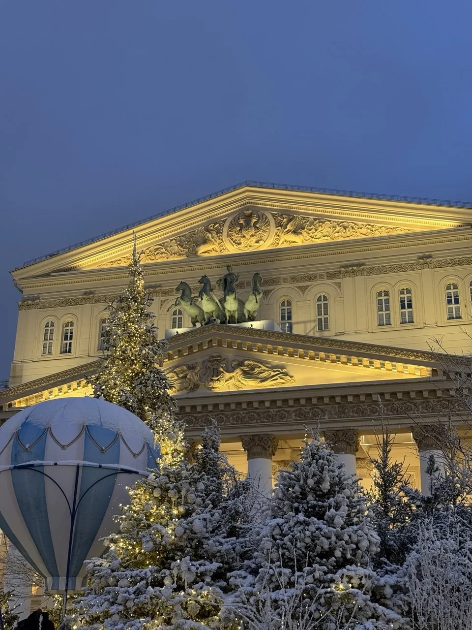 La façade du Bolchoï illuminée au crépuscule, un sapin devant