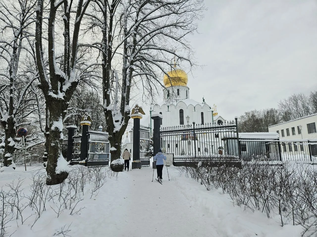 Une église blanche à coupole dorée sous la neige, des skieurs de fond sur le chemin